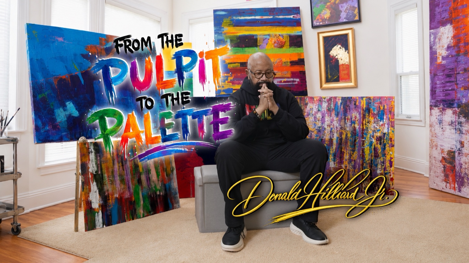 Bishop Donald Hilliard, Jr. seated among his vivid abstract paintings, beside the hand-painted title From the Pulpit to the Palette and his gold signature.